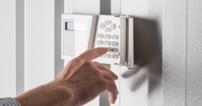 person typing on keypad of home burglar security alarm img